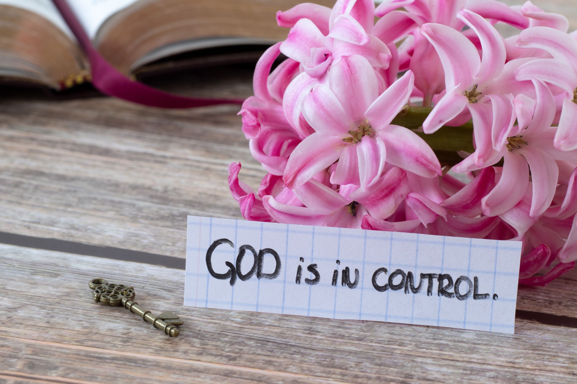 God is in control, handwritten quote with flower, ancient key, and open holy bible book on wood